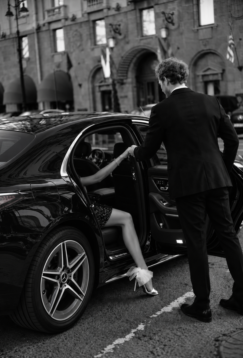 Black-and-white photograph of a chauffeur helping a woman out of a Mercedes-Benz.