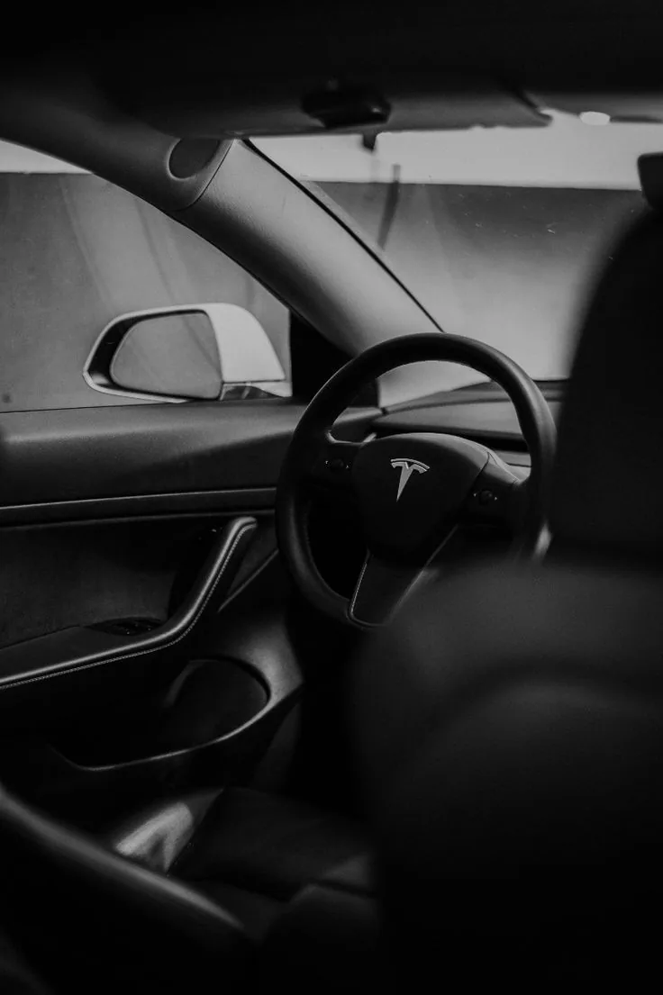 Black-and-white photograph of a Tesla interior, showing the steering wheel.