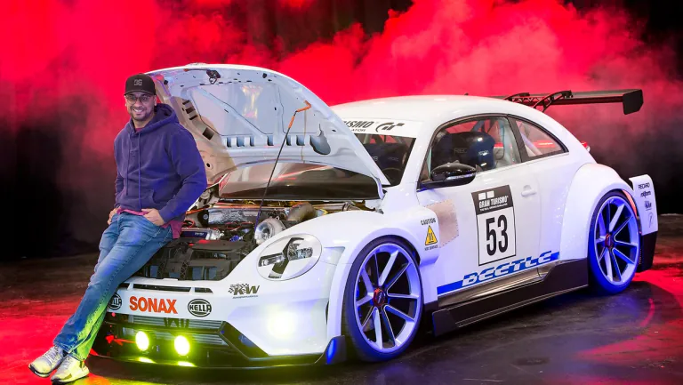 A man beside a white modified car with its bonnet open against red smoke.