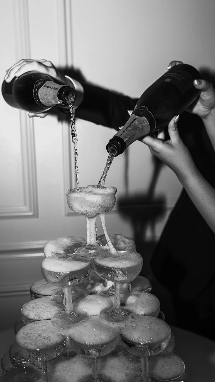 Champagne being poured into the top glass of a champagne tower.