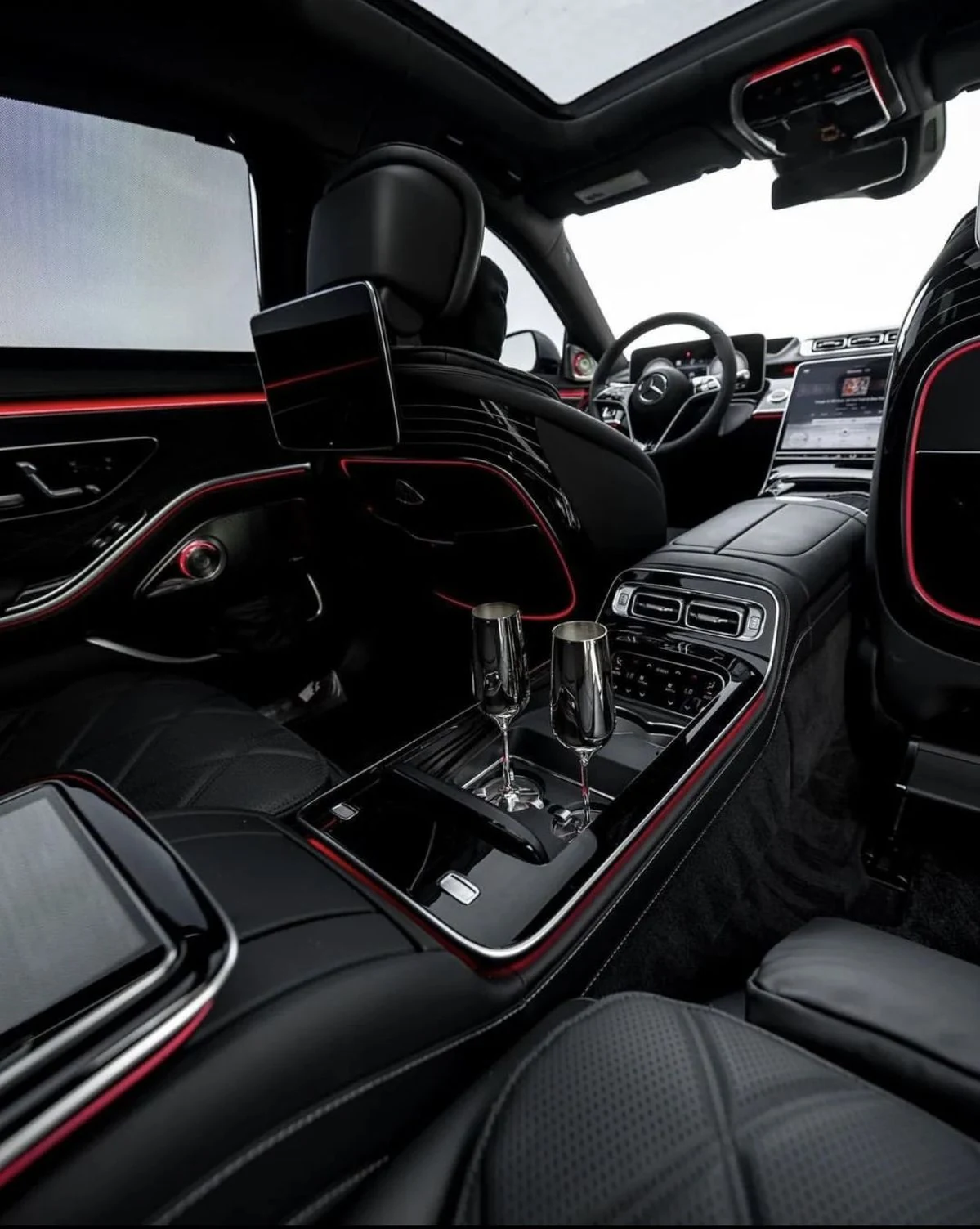 A Mercedes-Benz cabin with dark leather seats and two glasses on the centre console.