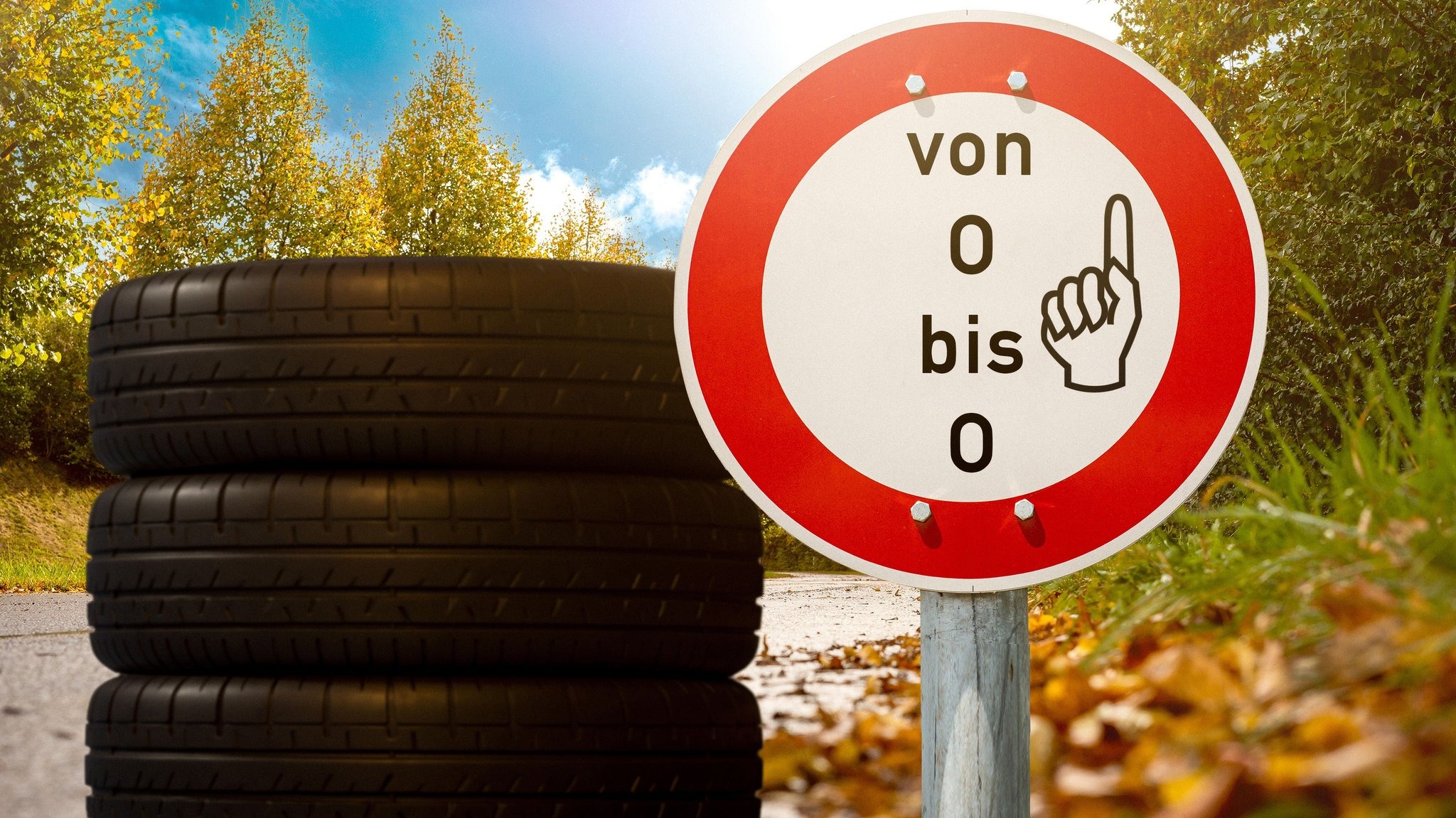 Stacked car tyres beside a sign reading “von O bis O” in an autumn landscape.
