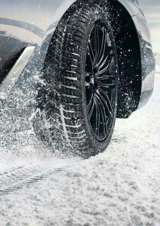 Close-up of a car tyre with a dark wheel rim and flying snow.