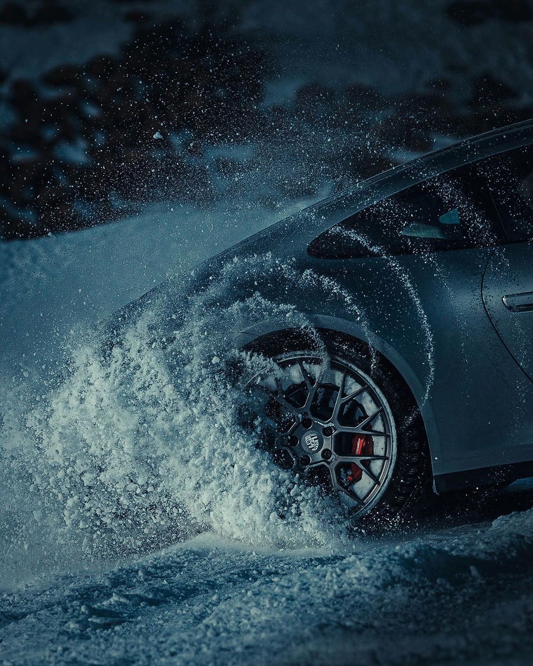 A car wheel and wheel arch surrounded by flying snow.