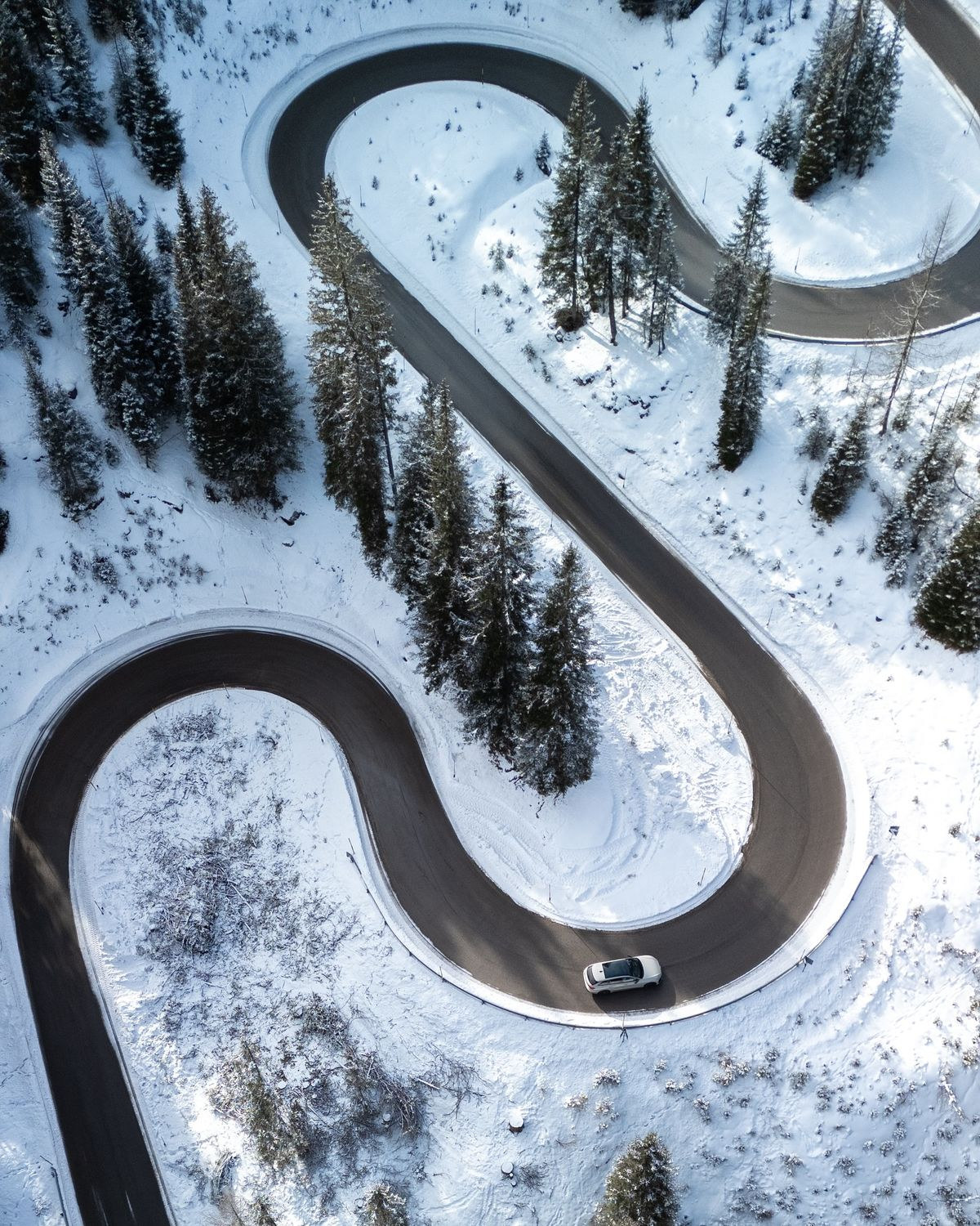 Aerial view of a winding road and a car in a snowy forest landscape.